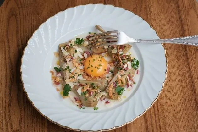 Alcachofas braseadas al vino blanco con vinagreta de jamón ibérico, yema de huevo, almendra y cebolla frita