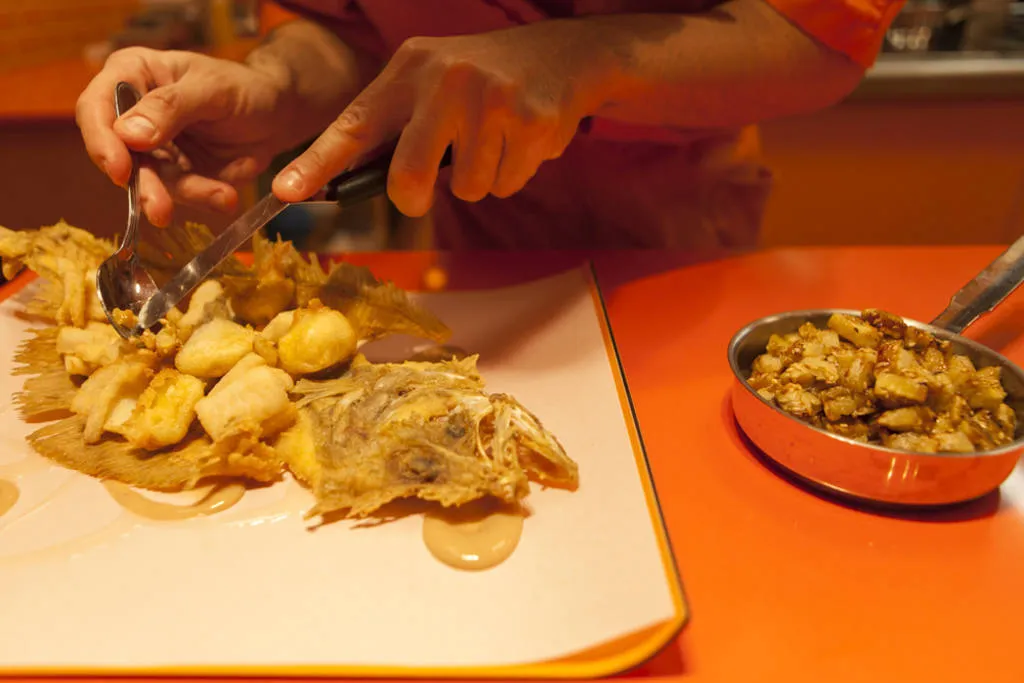 Sobre la espina frita del gallo sirve los cubos de gallo acompañados de salsa de tamarindo, cubos de plátano asados, puré de plátano y hojas de menta, albahaca y cilantro. Sal-pimenta y sirve.