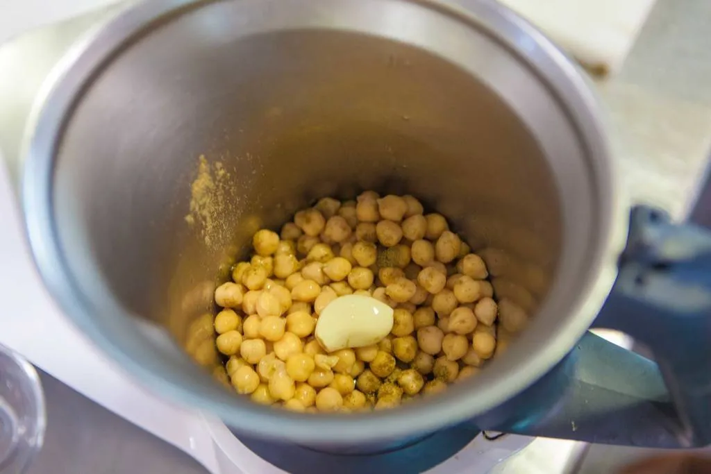 Mezclar los garbanzos, el ajo, el zumo de limón, un poco de comino y la sal y triturar con la batidora o la thermomix. Añadir poco a poco el aceite de oliva y el de sésamo, sin dejar de triturar, para que vaya emulsionando. Una vez conseguida la textura deseada, se reserva el hummus.