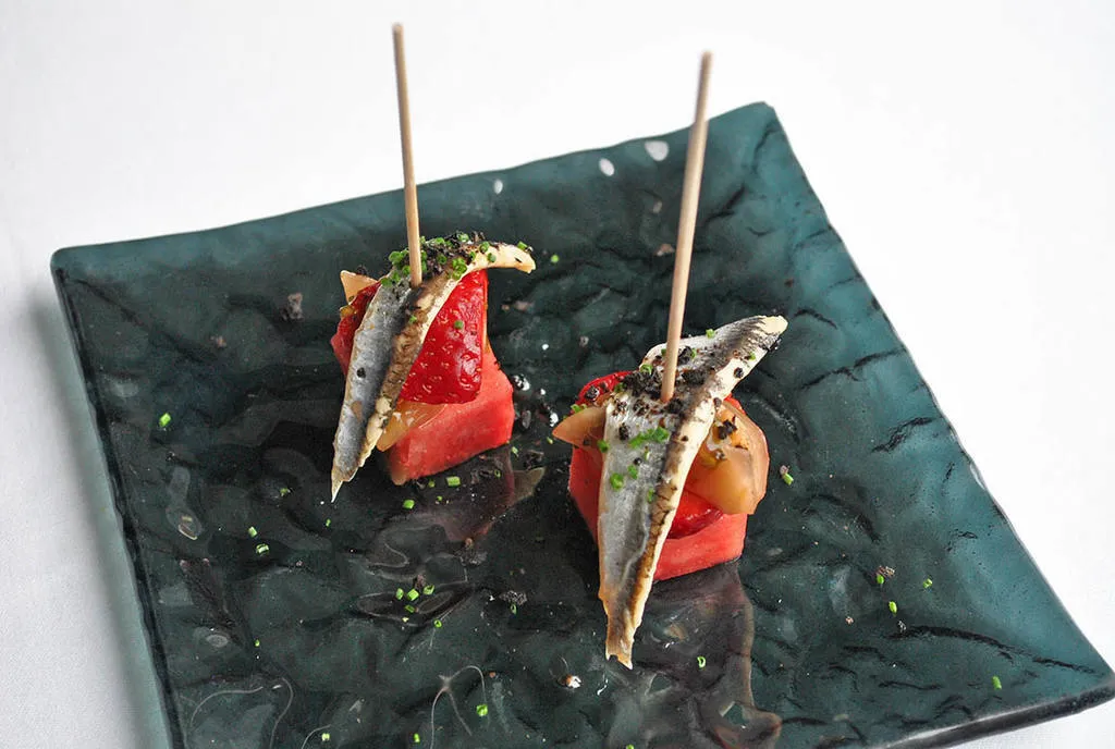 Brocheta de sandía marinada con vinagre de frambuesa, tomate kumato y boquerón.