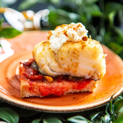 Tostada de pan mallorquín con tomate, pimientos asados, bacalao rebozado con panko, alioli y una pizca de pimentón rojo picante