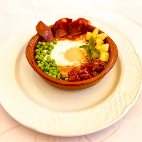 Cazuela de tomate casero con huevo cuajado acompañado de jamón, guisantes, chorizo y patatas