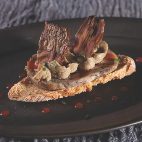 Base de pan, cordero a baja temperatura, crema de champiñones, chalota y alcachofa crujiente