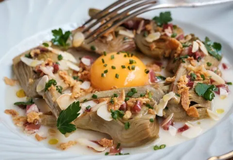 Alcachofas braseadas al vino blanco con vinagreta de jamón ibérico, yema de huevo, almendra y cebolla frita